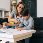 Matka s dítětem se společně učí v obývacím pokoji, sedí u stolu